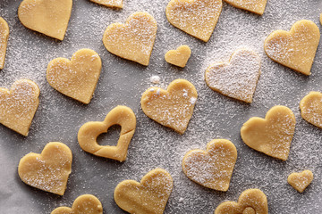 uncooked heart shaped cookies on parchment white paper sprinkled with powdered sugar