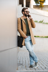 Image of man talking on smartphone and standing by building outdoors