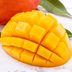 Fresh mango,beautiful chopped fruit with green leaves on bright wooden table background. Tropical fruit design concept, close up, copy space.