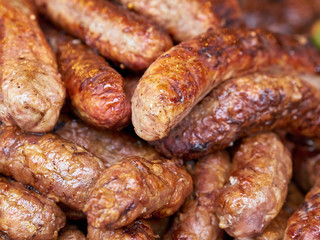 Heap of freshly grilled chicken or pork meat sausages at street food festival, selective focus, close-up. Unhealthy oily barbeque street fast food for meat lovers concept