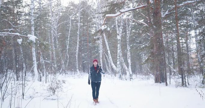 A man lumberjack is walking with an ax through a snowy forest. Stops and looks around.