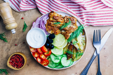 Lunch bowl with grilled chicken, red onion, tomato, cucumber, lemon, olive and sause on wooden background. Top view.