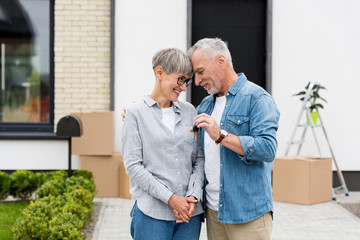 mature man holding keys of new house and hugging smiling woman