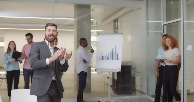 Multi ethnic office workers greeting new corporate ceo entering room. Male and female business staff applouding, cheering to colleague. Camera view. Indoors.