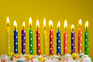 multi-colored candles burn on a birthday cake on a yellow background