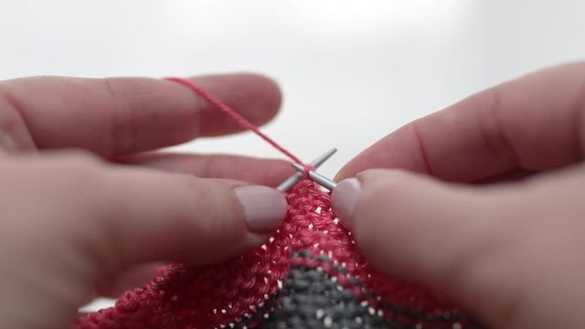 Nahaufnahme von weiblichen H&auml;nden, die aus rosa, magenta Wolle aus Baumwolle mit Stricknadel stricken.