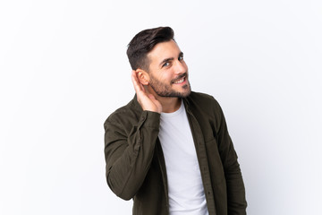 Young handsome man with beard over isolated white background listening to something by putting hand on the ear