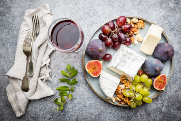 Camembert or brie cheese with fresh figs, honeycomb and glass of wine on plate over gray backdrop, top view, copy space