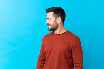 Young handsome man with beard over isolated blue background looking to the side