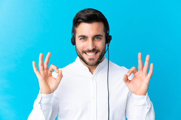 Naklejka premium Telemarketer man working with a headset over isolated blue background showing an ok sign with fingers