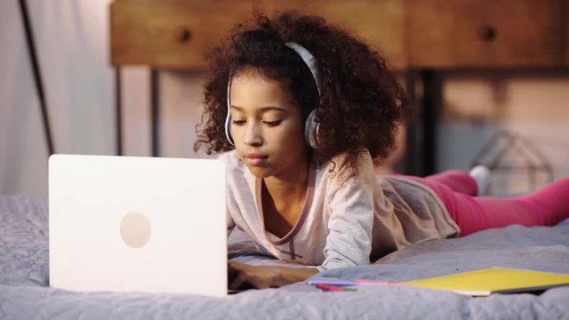 african american child doing homework on laptop in bed