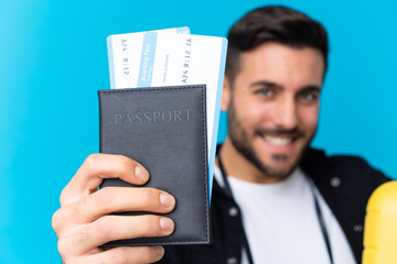 Traveler man holding a suitcase and a passport over isolated blue background
