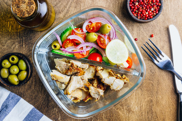 Healthy lunch box with chicken, tomatoes, cucumbers, olive and onion on wooden table. Top view