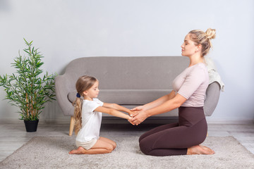 Young mother and little daughter keeping eyes closed sitting on floor, holding hands together and...