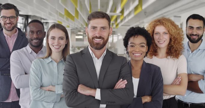 Portrait of smiling business staff team looking to camera and crossing hands. Close up view of positive group of diverse coworkers smiling and standing in modern businesscentr. Concept of teamwork.