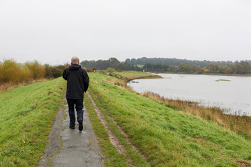 A middle aged man walking along a river path while talking on his mobile phone