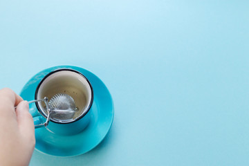 Blue background, strainer and a cup of green tea, a woman's hand makes tea