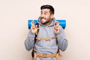 Young mountaineer man with a big backpack over isolated background with fingers crossing