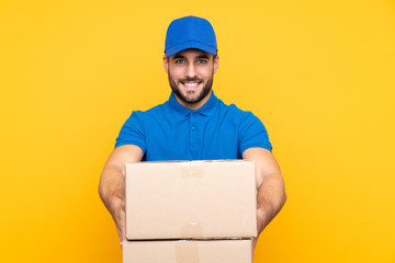 Delivery man over isolated yellow background with happy expression - obrazy, fototapety, plakaty