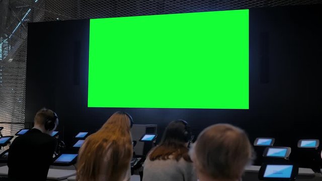 Group of students looking at large wall blank interactive green display at modern technology exhibition or museum. Mock up, green screen, futuristic, copyspace, template, education, chroma key concept