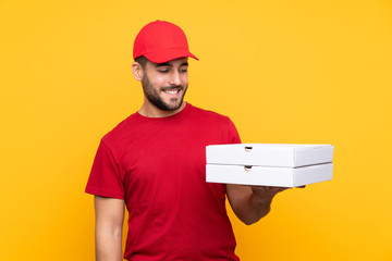 pizza delivery man with work uniform picking up pizza boxes over isolated yellow background with happy expression