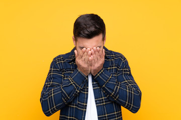 Young handsome man with beard over isolated yellow background with tired and sick expression