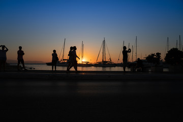 Fototapeta na wymiar Silhouettes of people admiring the sunrise and yacht masts all back-lit by golden glow