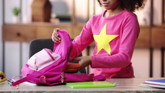 partial view of african american child putting books in backpack and walking away