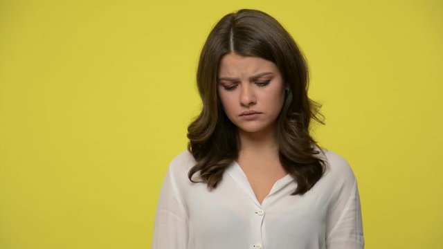 Upset young woman with brunette hair in blouse looking at camera with frustrated resentful expression, feeling depressed offended, is about to cry. indoor studio shot isolated on yellow background
