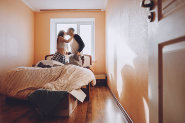 Happy young couple is having fun in bed in new empty home. Enjoying the company of each other. Pillow battle. Valentine's Day