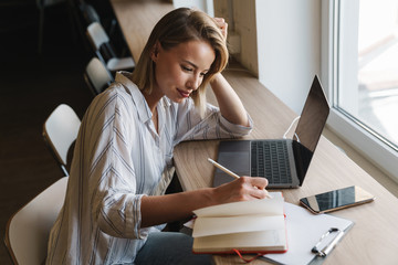 Photo of pleased blonde woman making notes while working