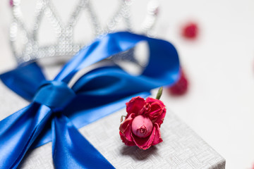 Gift box with blue bow of satin ribbon. Red rose on it. Silver crown in the background