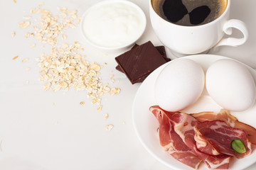 breakfast of black coffee, meat, eggs and chocolate close-up