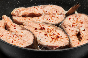 Salmon steaks in a pan with spices. Red fish on a dark background