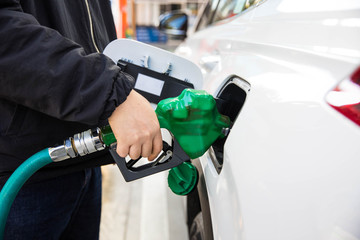 Hand holding a green filling gun while filling the fuel to a white car.