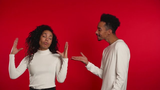 African woman showing bla-bla-bla gesture with hands and rolling eyes while boyfriend trying to say something. Couple isolated on red background. Empty promises, blah concept. Lier.