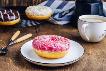 Colorful Donuts breakfast composition with different color styles of doughnuts and fresh coffee on wooden background. Selective focus