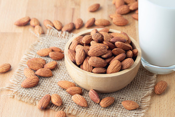 Almond seeds in a bowl wood on the sackcloth And a glass of milk on table wooden background