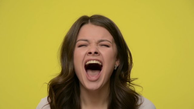 Closeup of angry brunette woman shouting with wide open mouth, showing rage and frustration, screaming aggressively, being pissed off yelling long and loud. studio shot isolated on yellow background