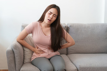 asian woman with menstruation and pain period cramps. young women having painful sitting on sofa at...