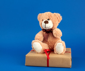 beige teddy bear and a box wrapped in brown kraft paper and tied with a red ribbon