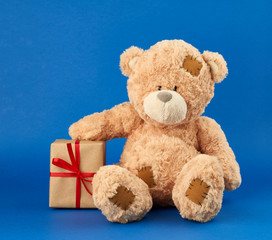 large beige teddy bear holds a box wrapped in brown paper and tied with a red ribbon