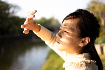 Asian child girl covering face by hand to protect,prevent face skin from bright sun in outdoor summer,female people hand covered the strong sun light feeling hot uncomfortable,risk of eyes damage