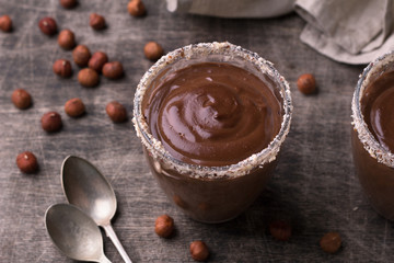 Chocolate mousse with cream and hazelnuts in glasses on old dark wooden table