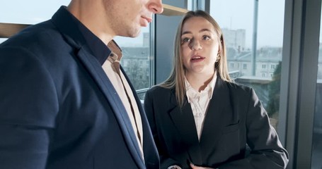 Man and a woman discussing work in the brightly lit modern office. Concerned male and female working with charts papers at hands. Standing business people discuss new startup project concept