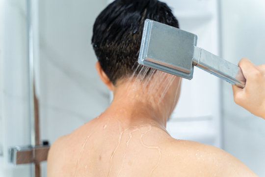 Back View Of Black Haired Undressed Man Pouring Hot Water From Shower Head In Modern Bathroom