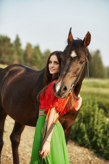 Gypsy girl rides a horse in a field in the summer. A woman with long hair strokes and caresses a horse standing in the green grass