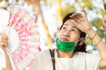Asian senior woman fanning and sweat on face suffer from sunburn very hot in summer weather problem...