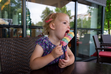 Cute blonde girl enjoying colorful ice cream on hot summer day at a bar.