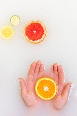 Orange in hands. Slice of green Lime and red grapefruit citrus fruits in murky muddy milky water.